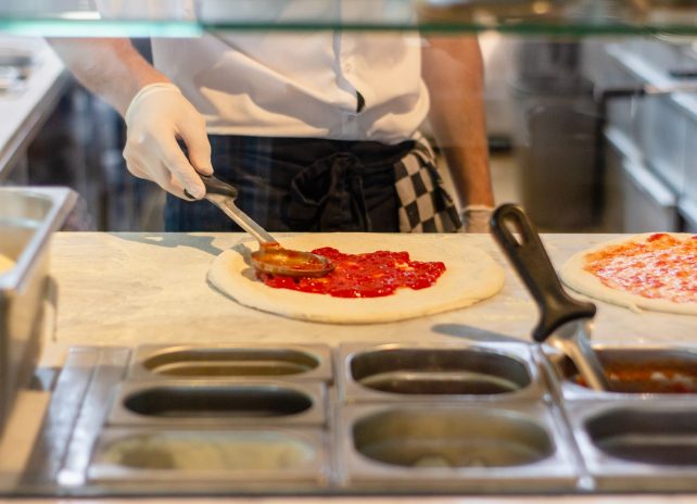 A Food Kitchen Chef Putting tomato Sauce On A Pizza Dough